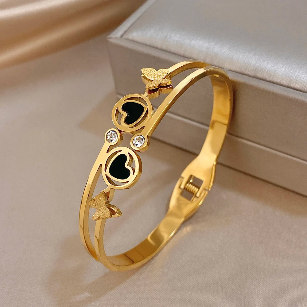 Gold-tone wide cuff bangle with black enamel heart circles, butterfly details, and stones