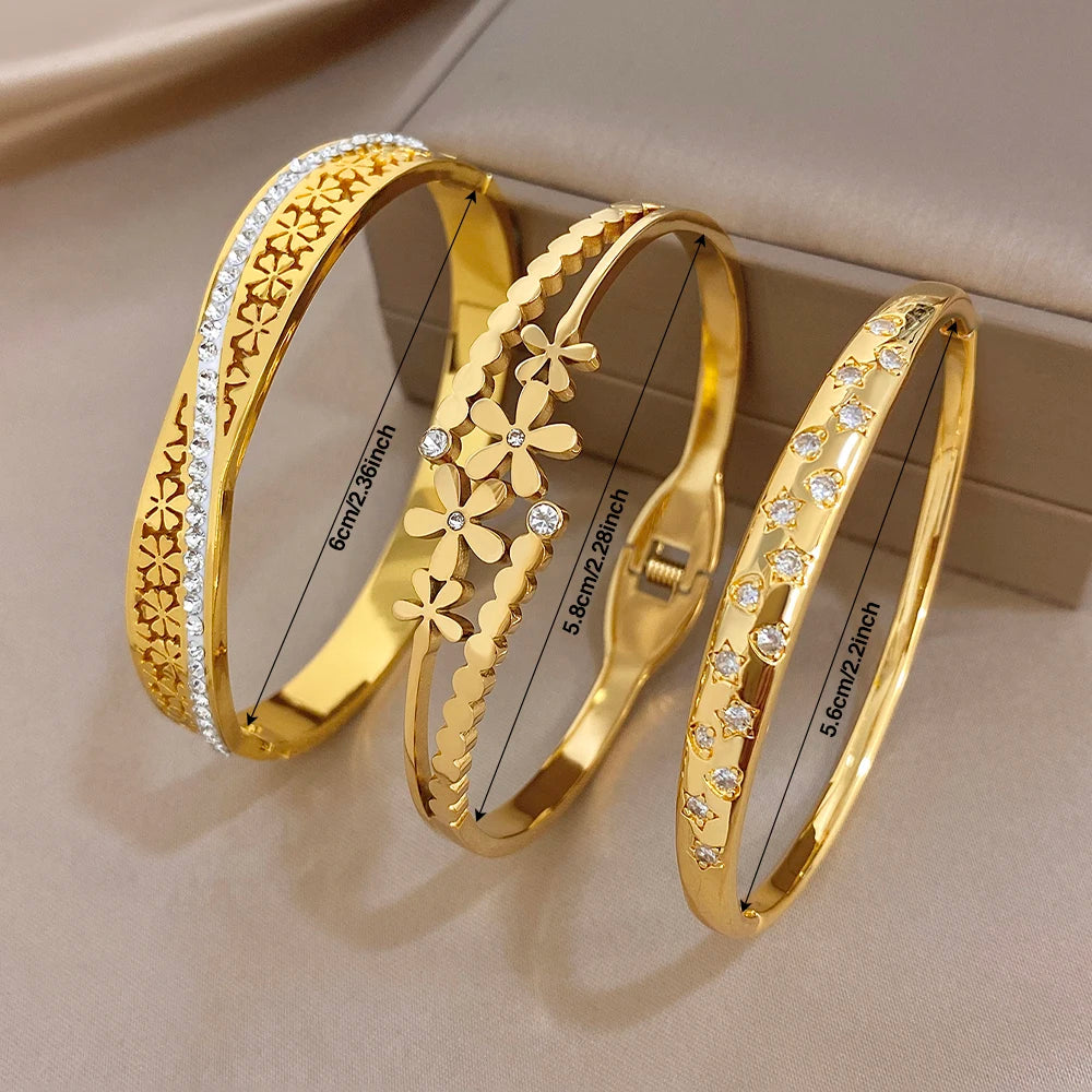 Three gold cuff bangles with engraved bands, daisy flowers, and clear stones