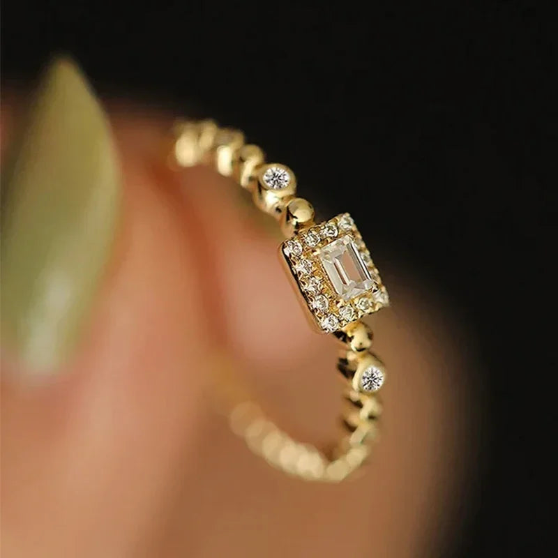 Gold-tone square halo ring with round accents on finger, angled close-up