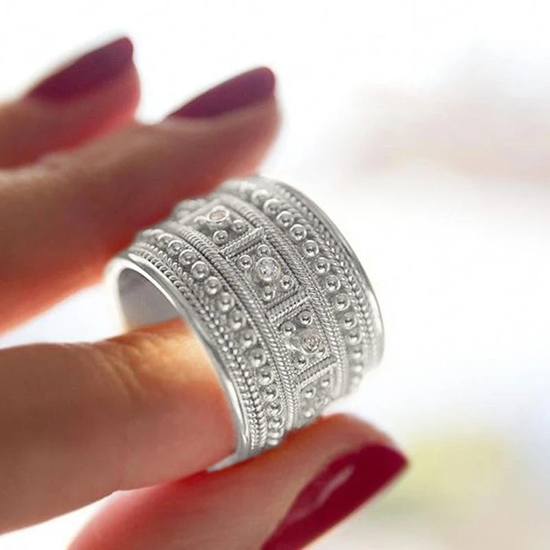 Silver-tone wide band ring worn on a finger, with detailed beading and clear stones