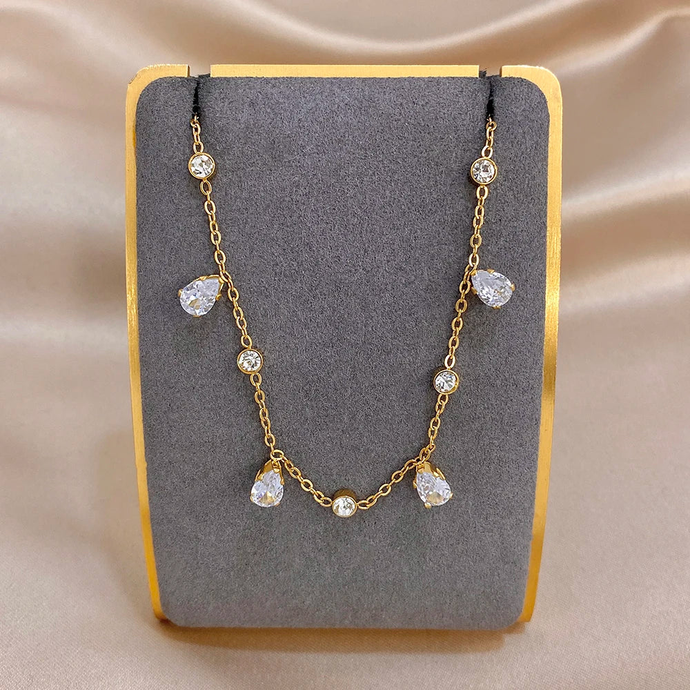 Gold-tone link bracelet with dangling teardrop zircon charms on display card