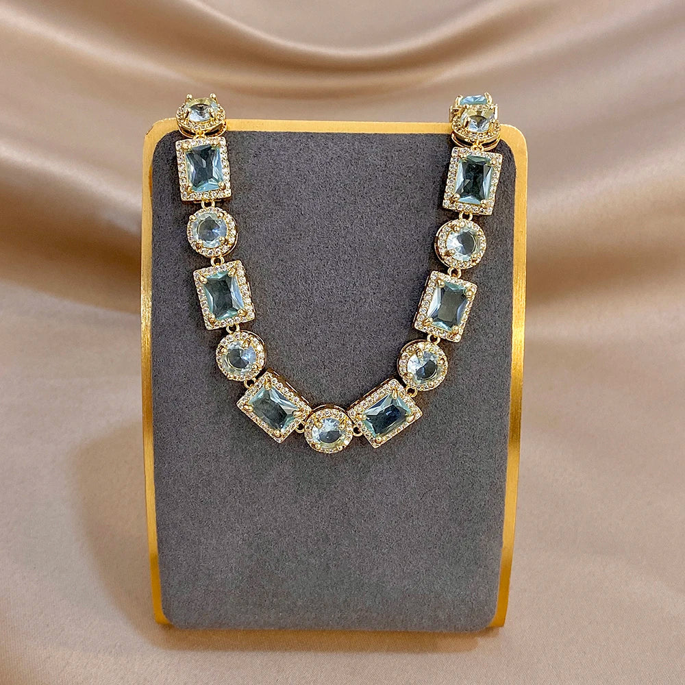 Geometric gold-tone bracelet with blue square and round stones on a display stand