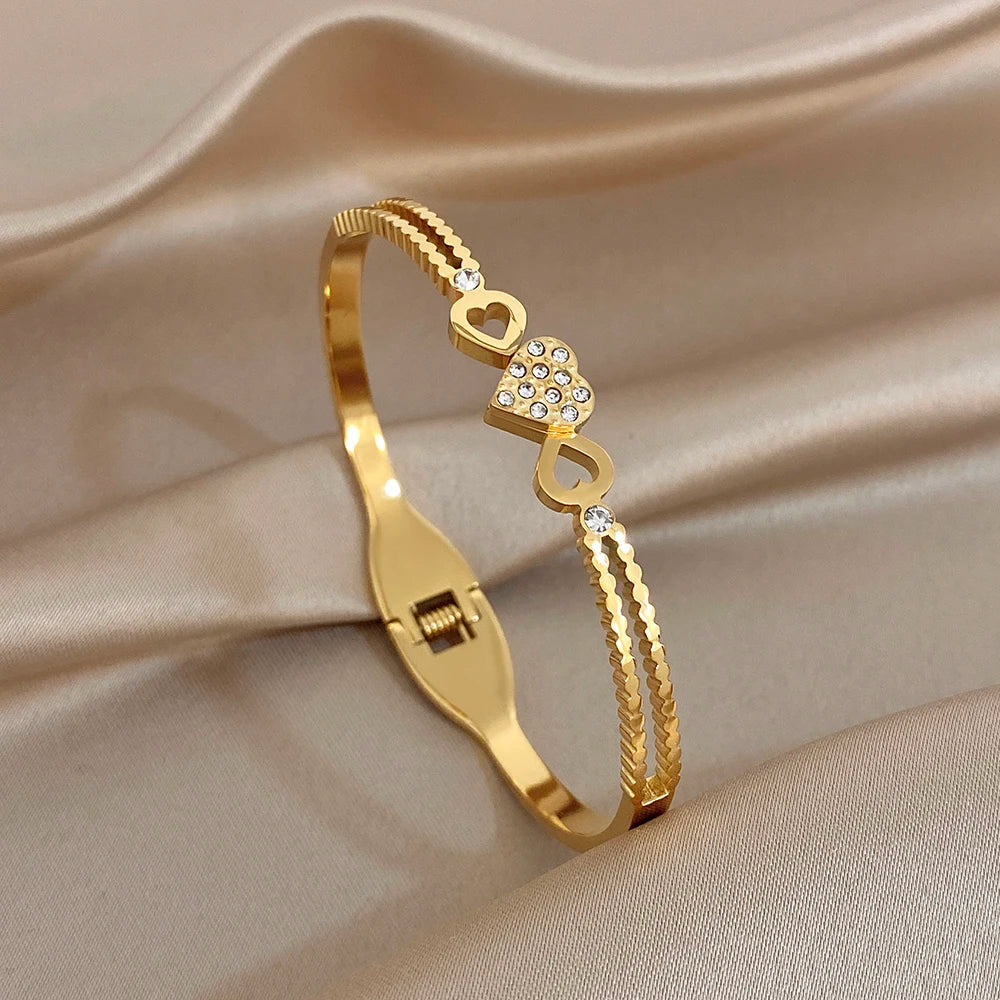 Gold-tone twisted knot heart charm cuff bangle with dangling braided detail and rhinestones