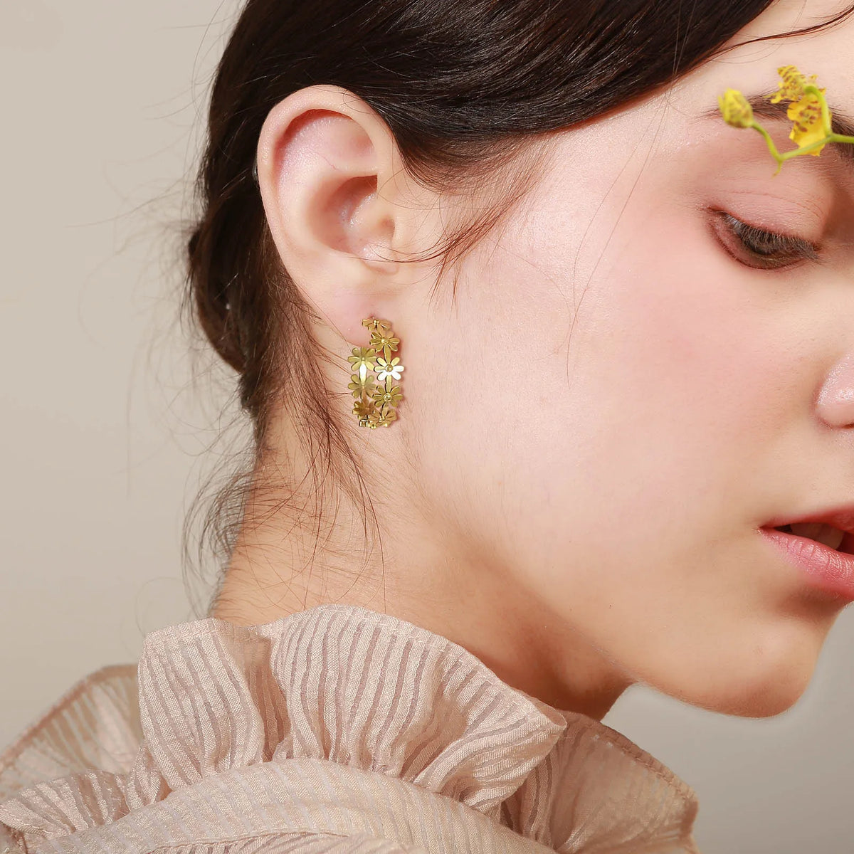 Gold-tone daisy flower hoop earrings worn on ear with dangling flower charm details