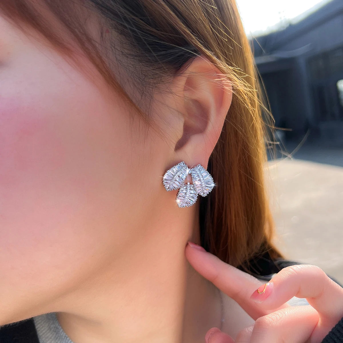 Silver-tone cubic zirconia leaf stud earrings worn on an ear, shown from the side.
