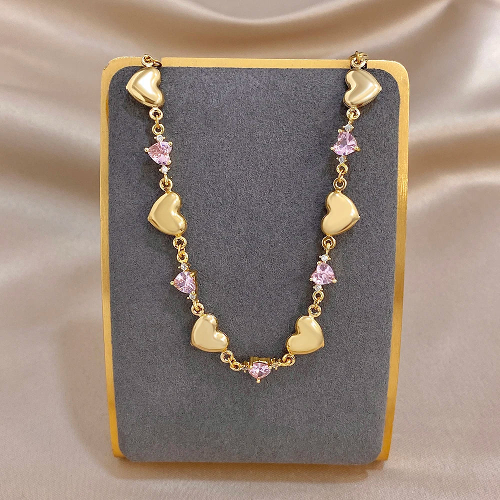 Gold-tone heart charm link bracelet with pink crystal-like stones, open circular shape