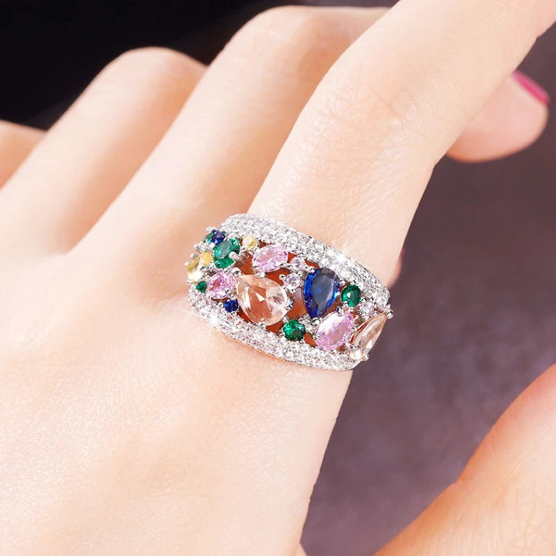 Silver-tone cubic zirconia ring with multicolor stones, shown on a hand close-up.