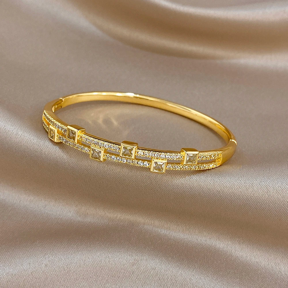 Gold-tone rhinestone cuff bracelet with square geometric links, side view on fabric