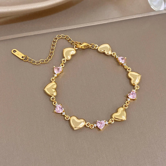 Gold-tone heart link bracelet with pink crystal-like stones along the chain