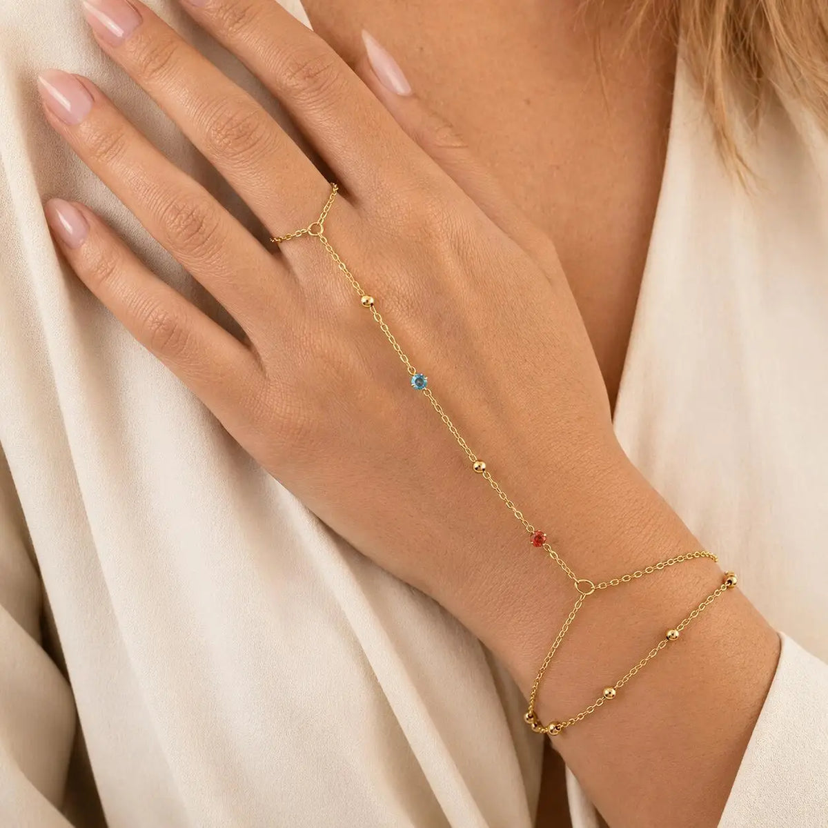 Gold-tone hand chain bracelet with blue and red CZ heart charms