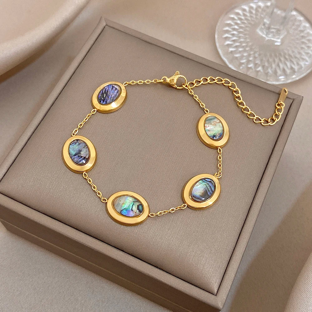 Gold plated oval charm bracelet with blue and iridescent abalone shell discs