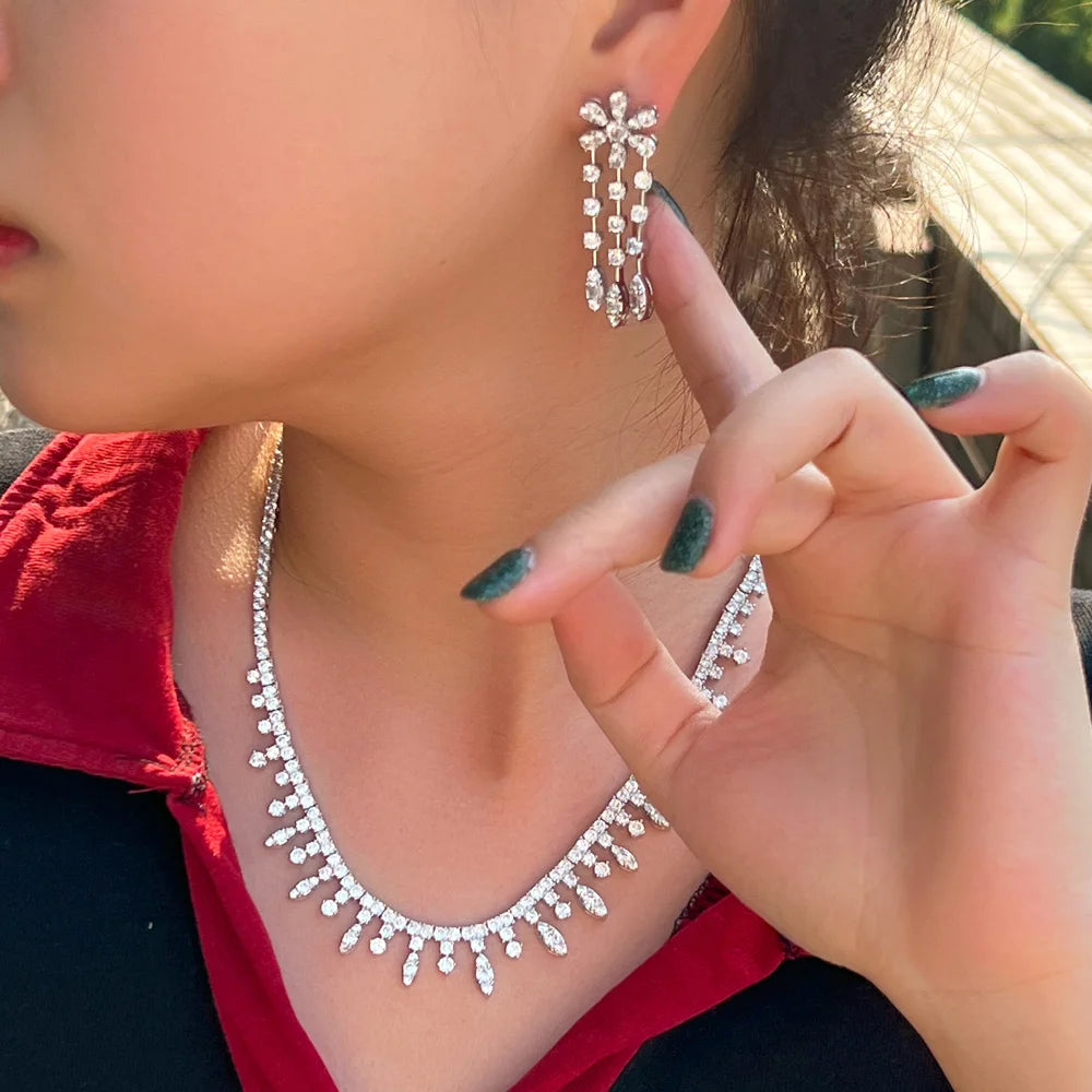 Woman wearing sparkling cubic zirconia necklace and floral drop earrings, silver-tone