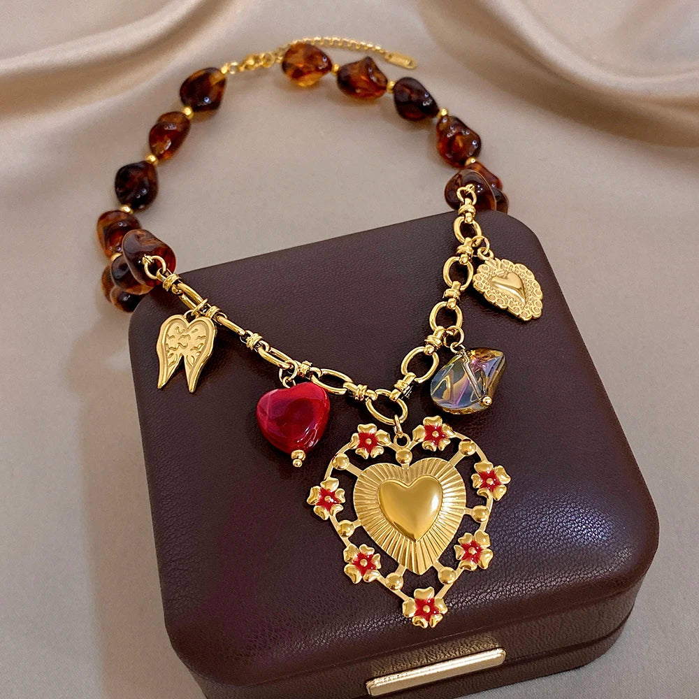 Gold-tone charm bracelet with amber beads, red heart charm, wing charms, and heart pendant
