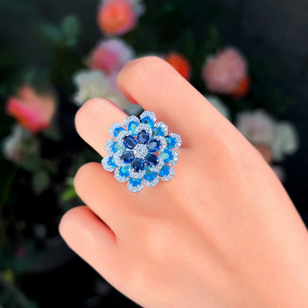 Layered blue floral ring with dark blue and pale blue stones, shown on hand