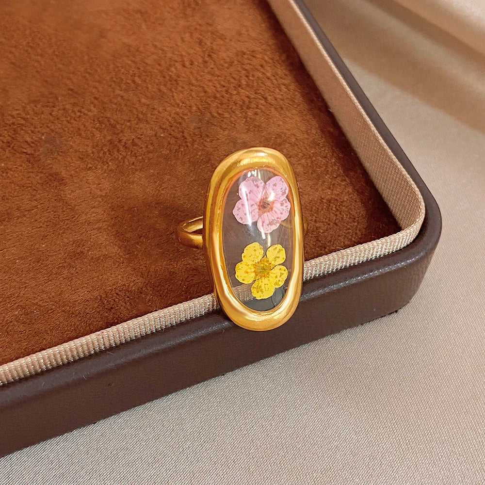 Gold-tone open oval flower ring on jewelry display with pink and yellow blossoms