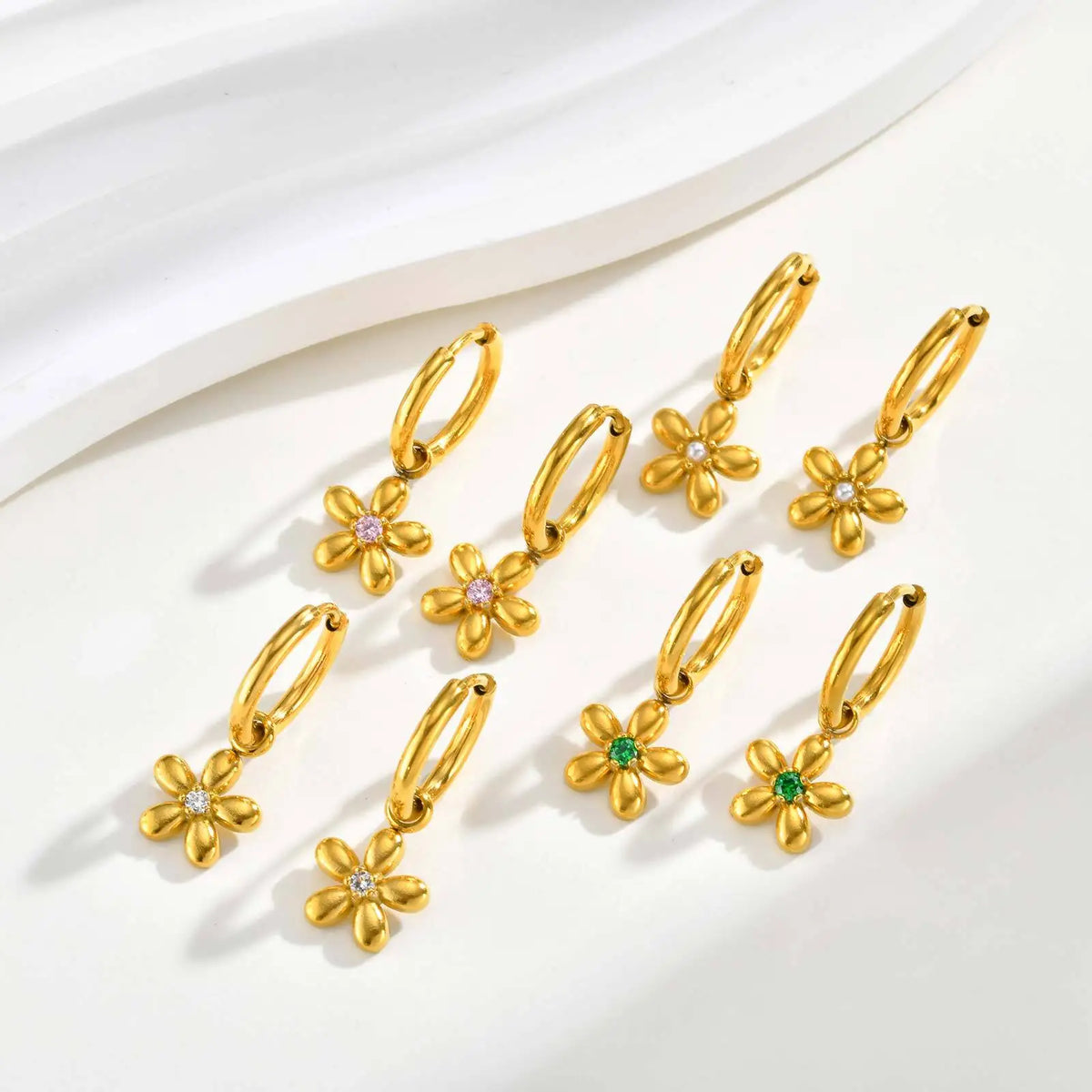 Gold flower charm hoop earrings displayed in clear and green center stone options.