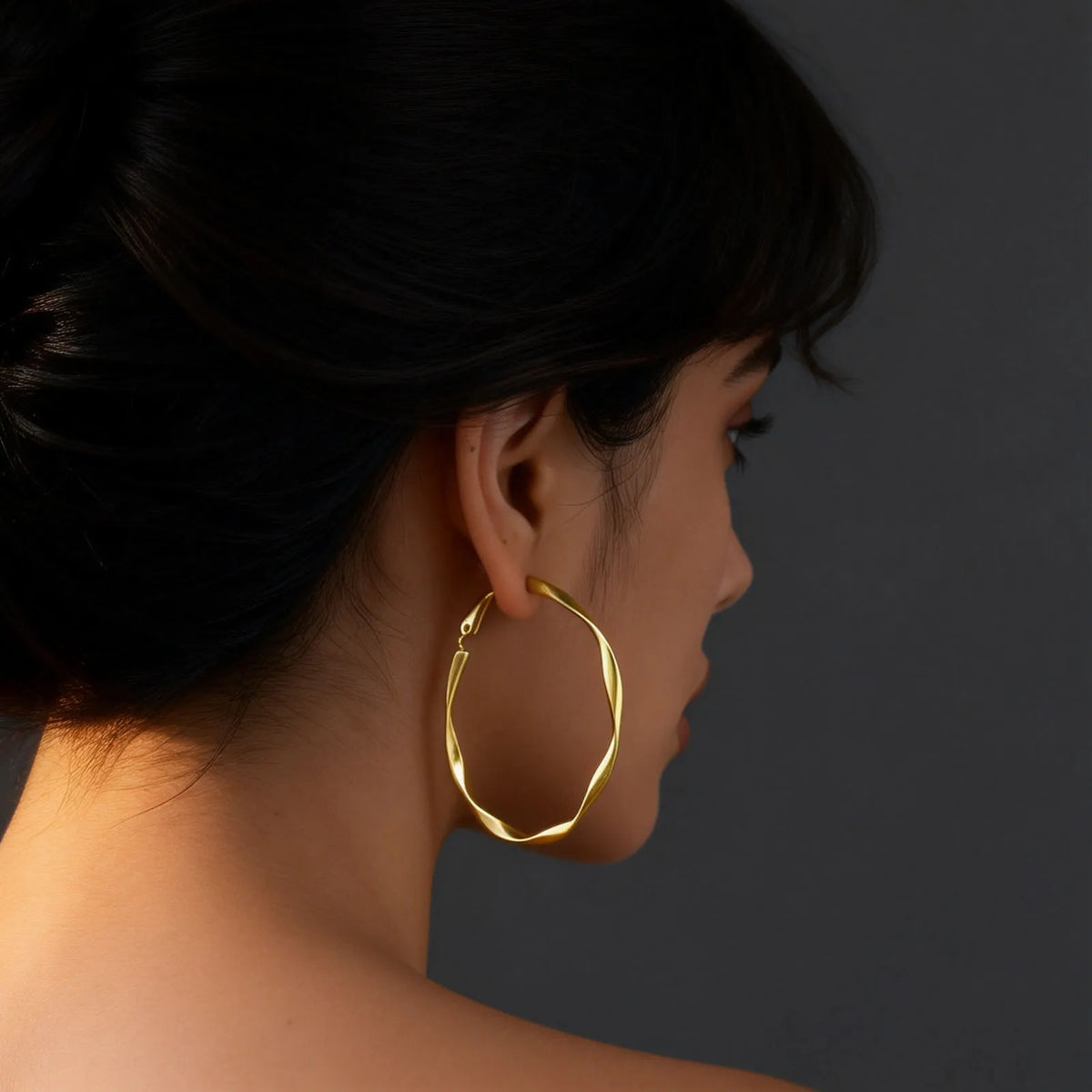 Gold-tone twisted hoop earring shown worn on an ear