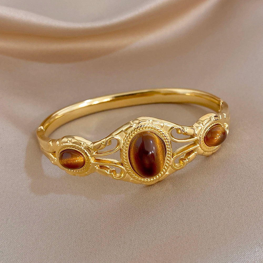 Gold-tone hinged cuff bracelet with oval brown tiger-eye cabochons and scrollwork
