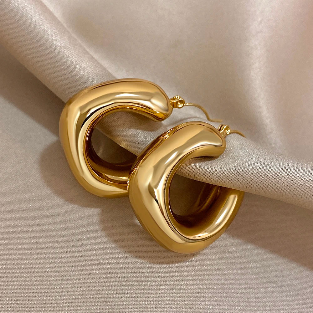 Close-up of thick, polished gold-tone hoops with open U-shaped fronts