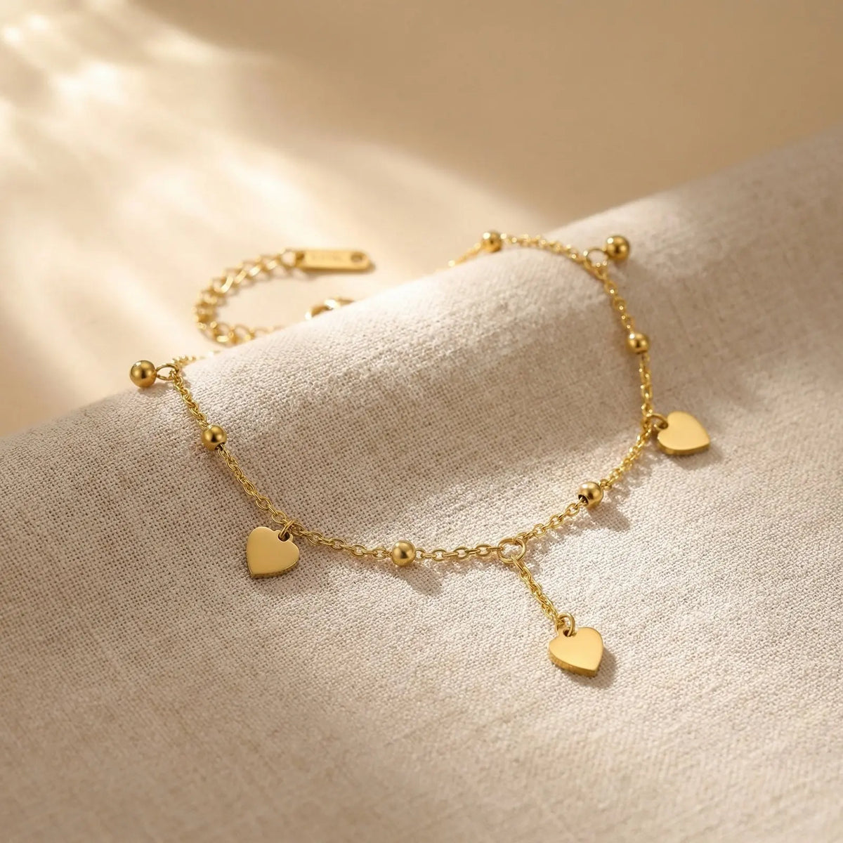 Gold heart charm anklet with beaded links and dangling heart charms on fabric