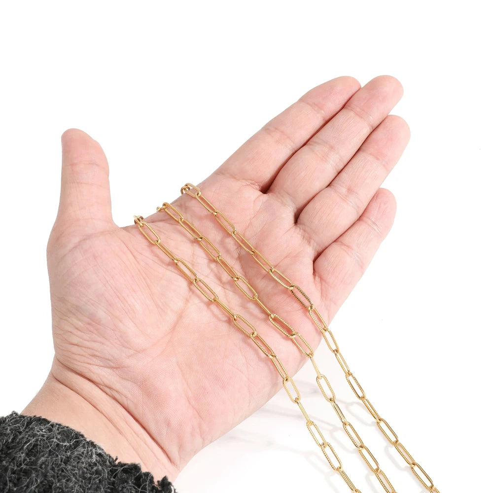 Gold-tone oval chain held in hand, cross/paperclip style flat links