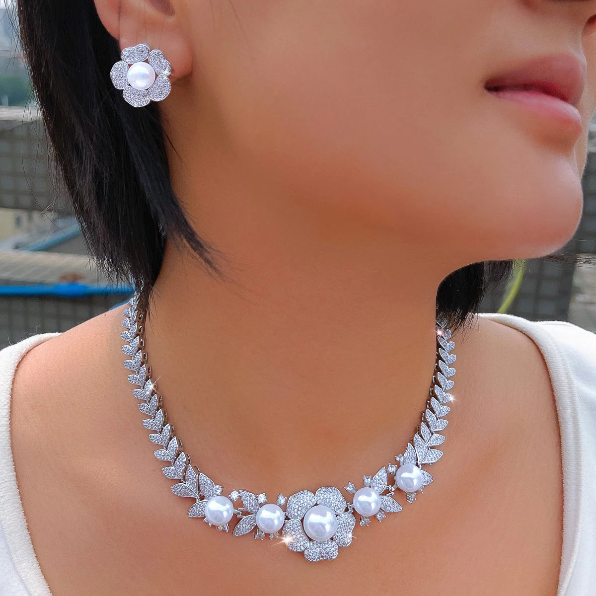 Close-up of pearl and cubic zirconia necklace and flower stud earring worn