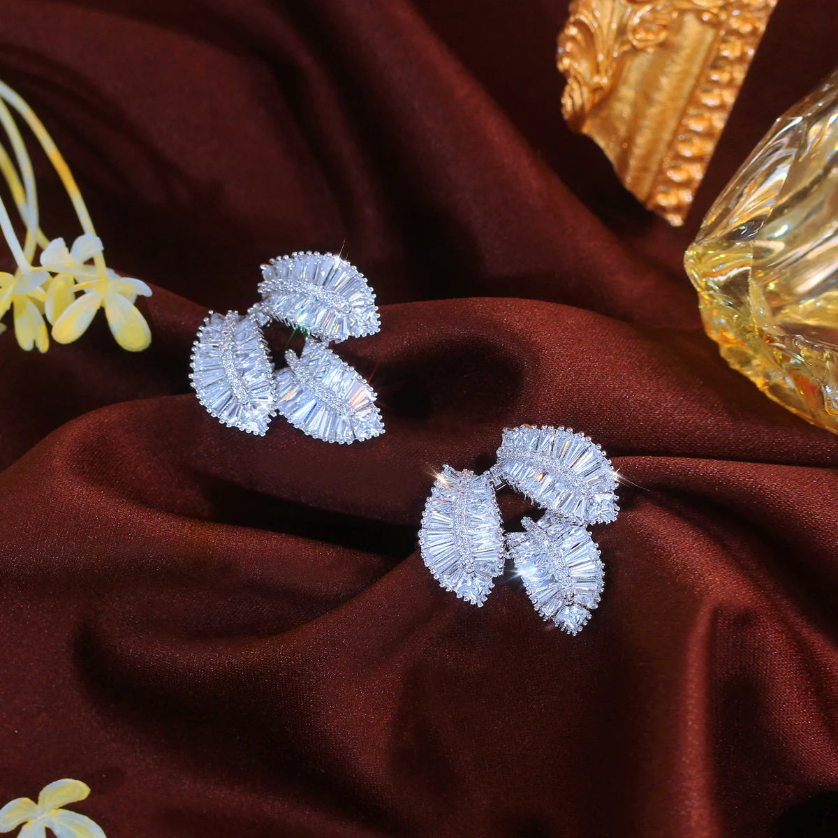 Silver-tone cubic zirconia leaf earrings shown at different angles, with three clustered leaves.