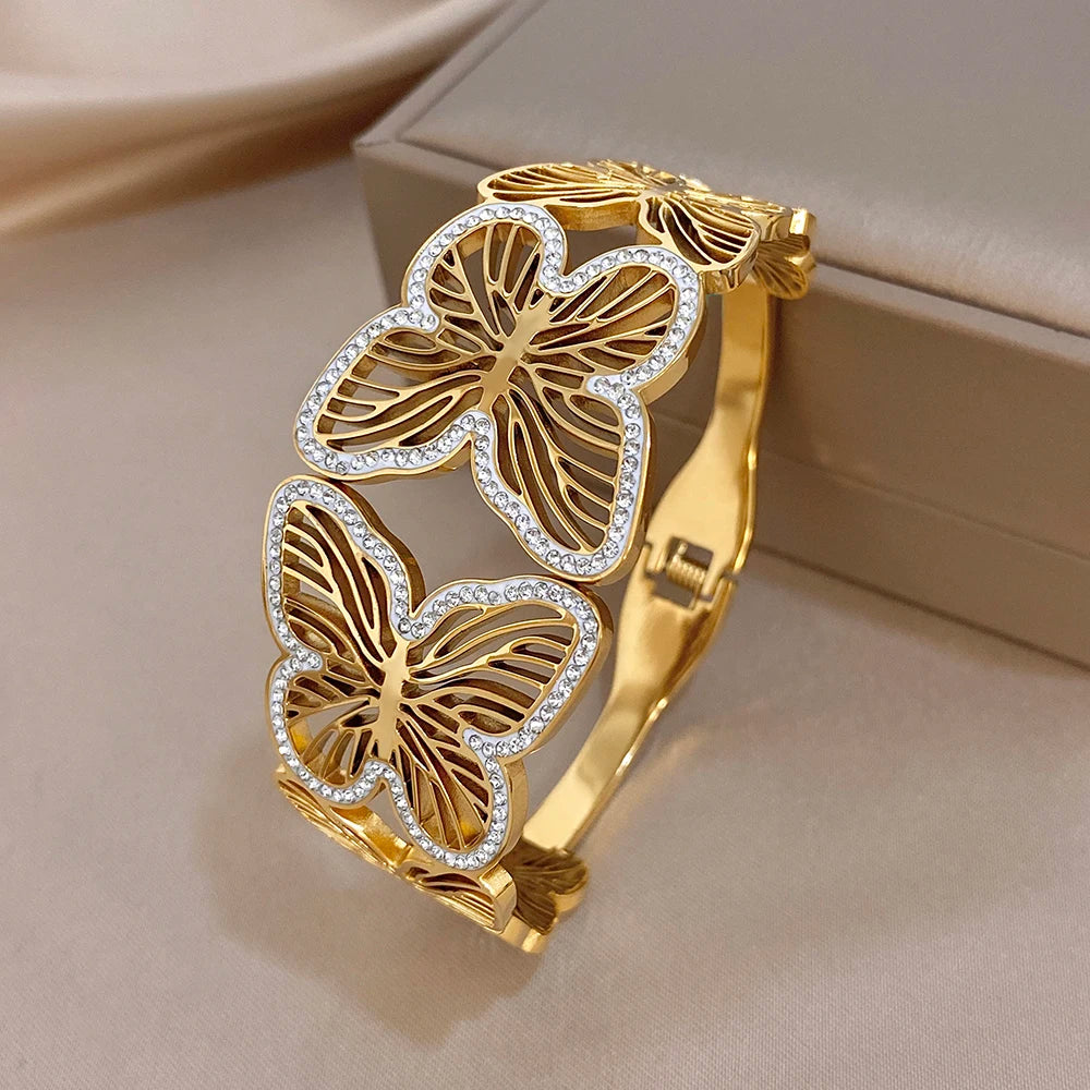 Gold-tone wide cuff bracelet with butterfly charms, rhinestone borders, and hinge clasp