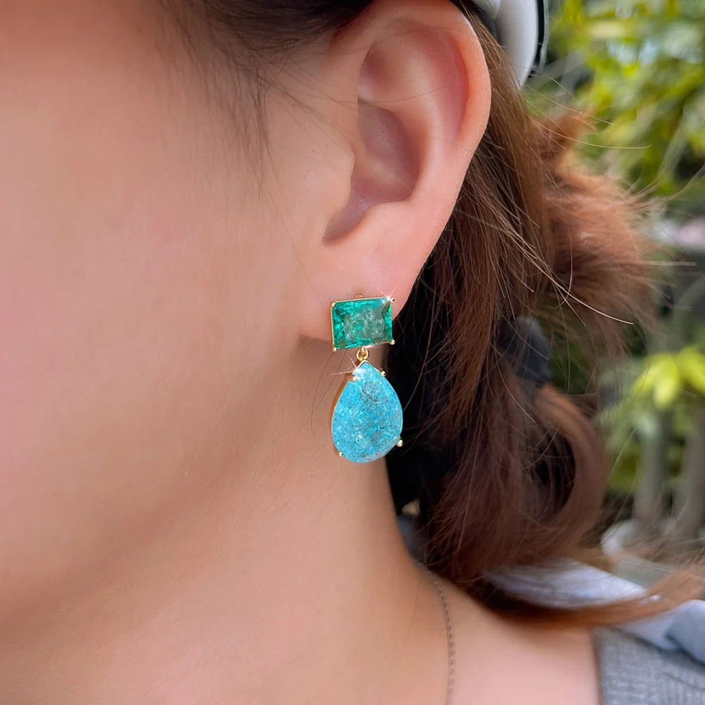 Close-up of a green square and blue teardrop drop earring worn on the ear