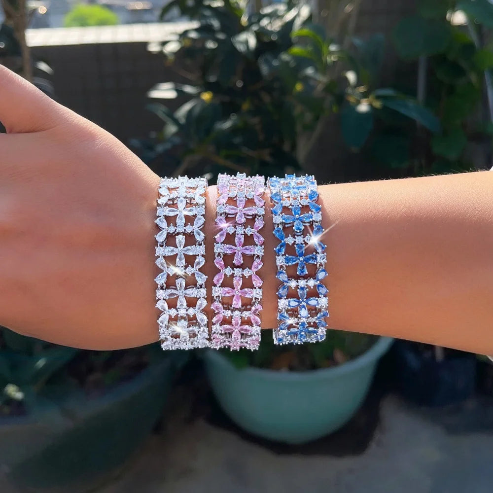 Three floral crystal tennis bracelets in clear, pink, and blue worn together on a wrist