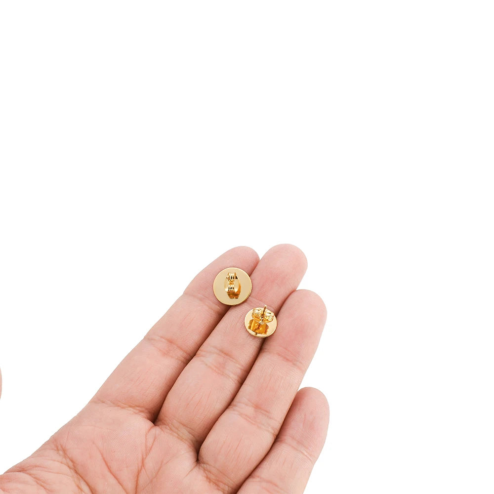Small gold round flat stud earring settings held in hand, blank bases with posts