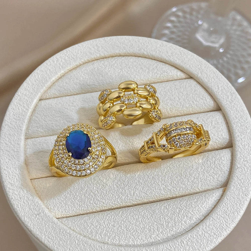 Gold-tone zircon rings in a round tray: blue oval ring and two clear crystal open bands