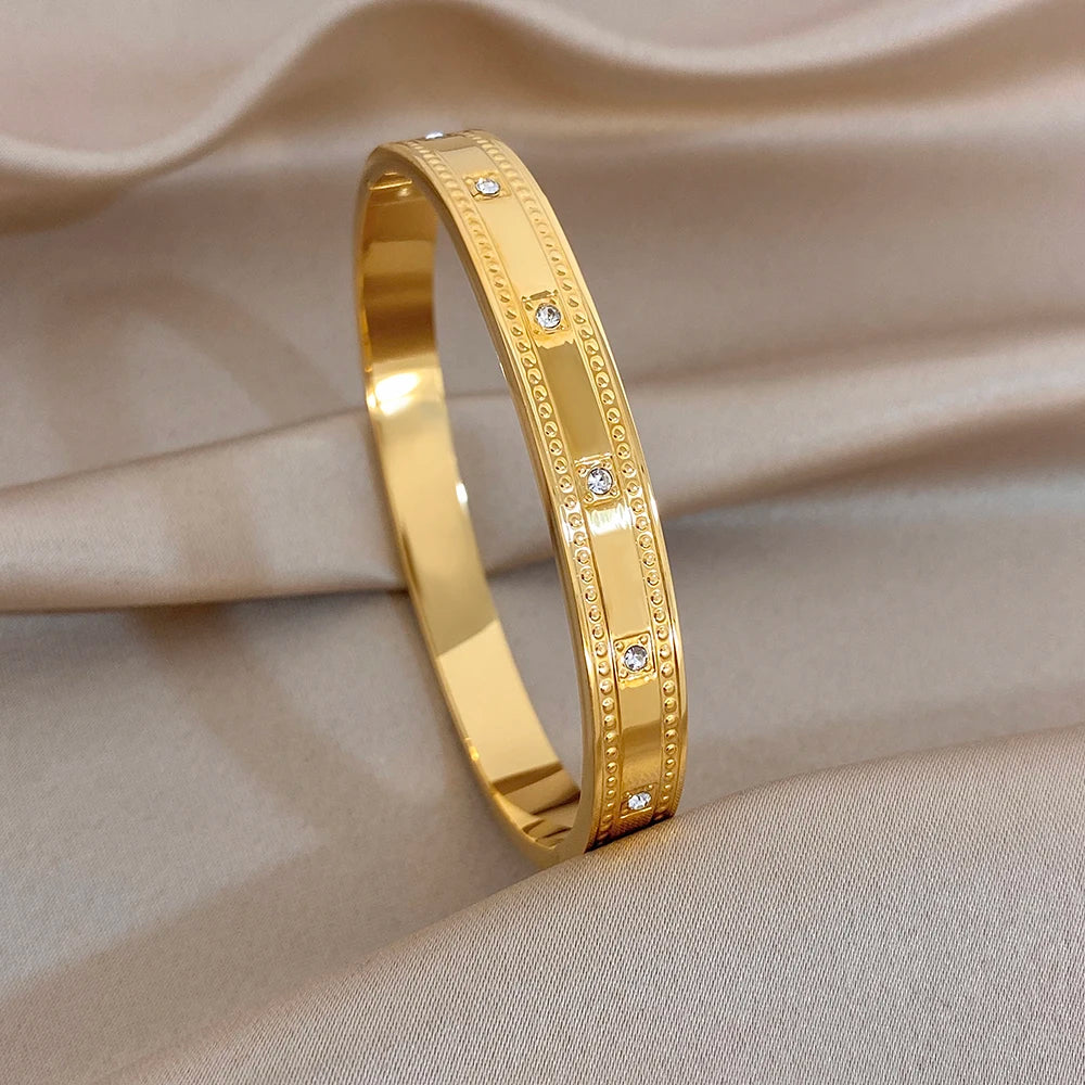 Gold tone slim cuff bangle with clear rhinestone bezel accents along the edge.
