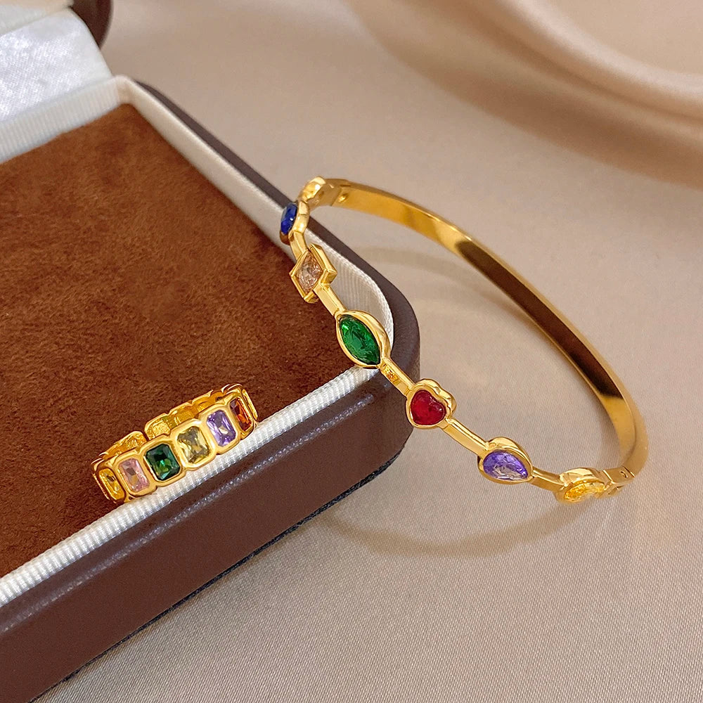 Gold-tone bangle bracelet with colorful bezel-set stones beside a matching band ring
