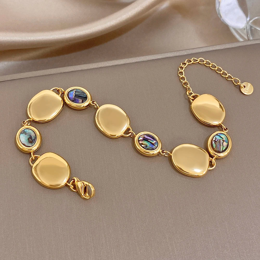 Gold-tone link bracelet with oval disc charms and iridescent abalone shell bead details