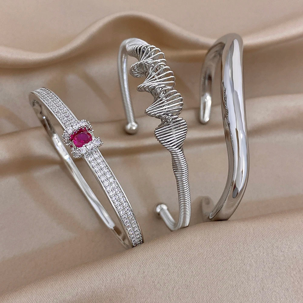 Silver cuff bracelet stack: textured wave band, plain cuff, and crystal red gemstone bangle