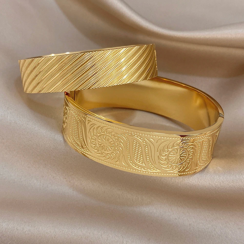 Gold-tone wide cuff bangle with engraved floral panels and diagonal textured lines
