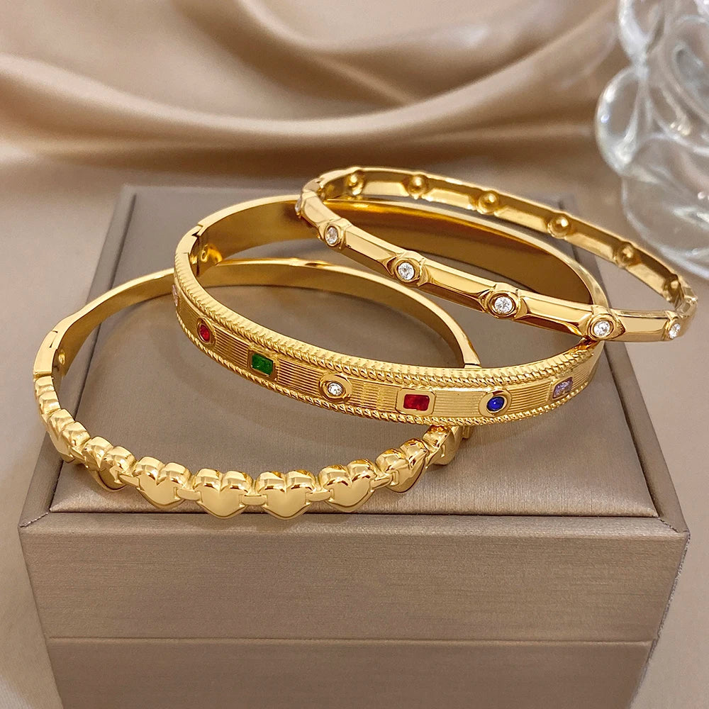 Gold-tone geometric and heart-link bangles with red, green, and blue gem accents