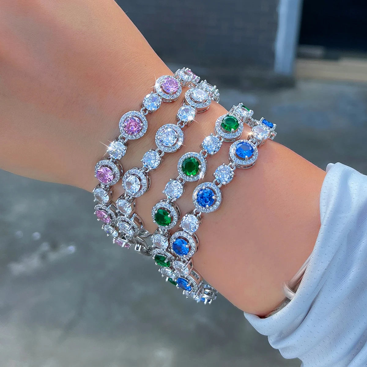 Silver-tone tennis bracelets with round clear, blue, green, and pink stones worn on a wrist