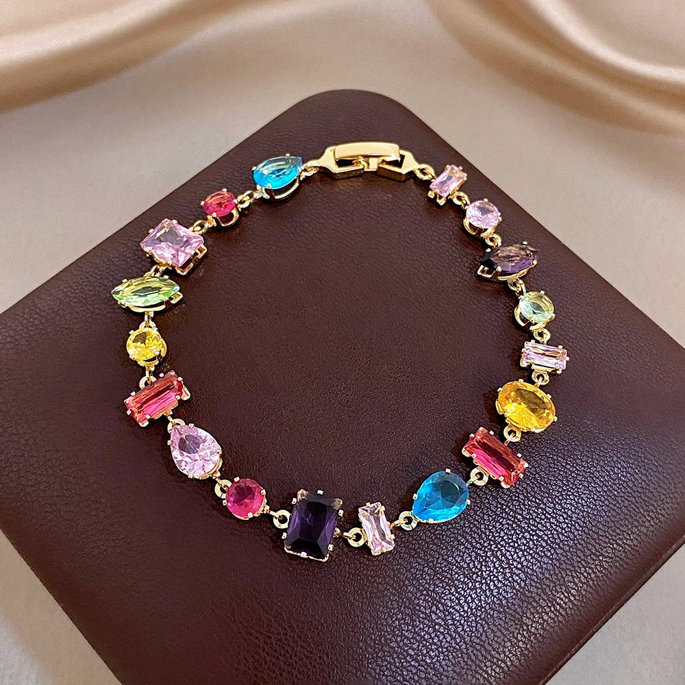 Multicolor zirconia link bracelet with gold-tone chain on dark faux leather backing.