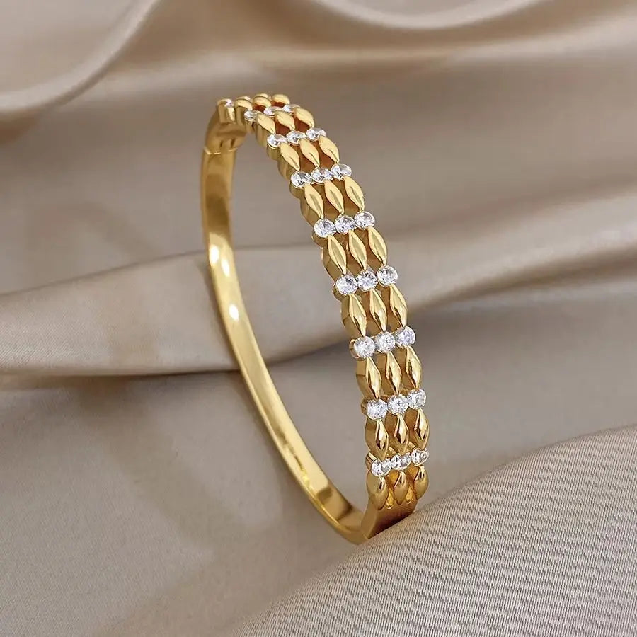 Gold-tone cuff bangle with textured link rows and clear round zircon-like stones