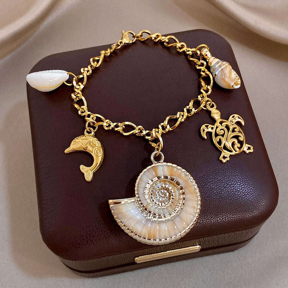 Gold-tone charm necklace and bracelet set with seashell spiral pendant, conch charm, and dolphin