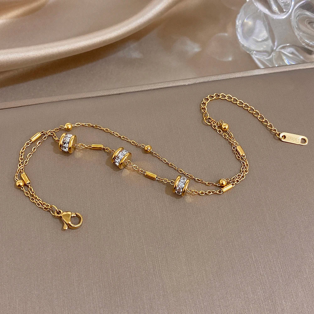 Gold double-layer chain bracelet with rhinestone bead charms and clasp, laid flat.