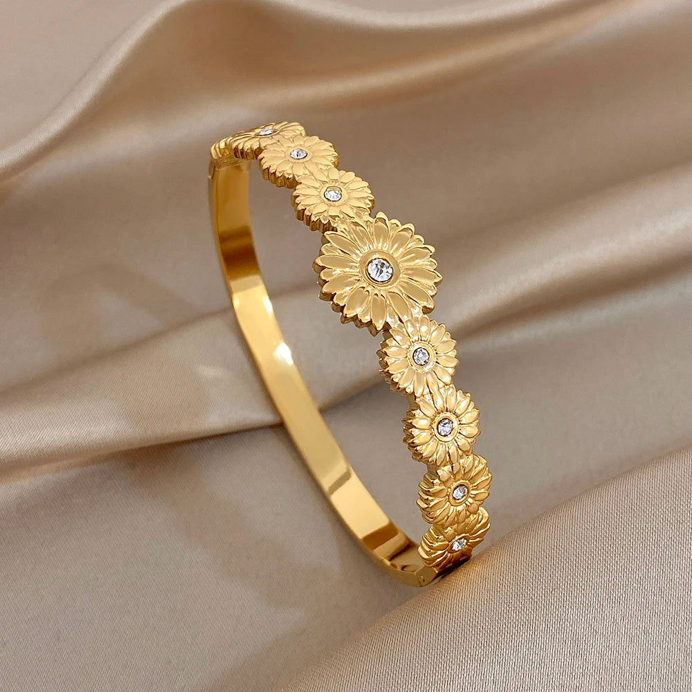 Gold tone cuff bangle featuring embossed floral row with clear rhinestone centers