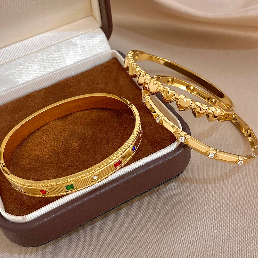 Gold-tone gemstone and heart-link cuff bangles in a jewelry box display