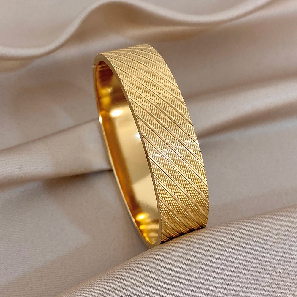 Gold-tone wide cuff bangle with textured geometric band and engraved flower panels