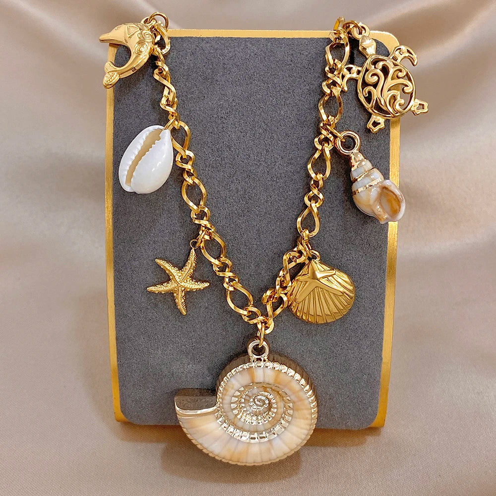 Gold-tone charm necklace and bracelet on box, featuring dolphin, shell, and ornate filigree charms
