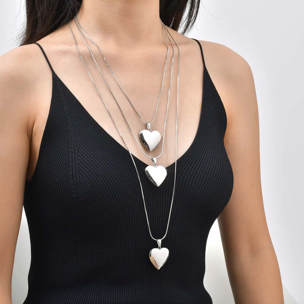 Silver heart sweater necklace with three heart charms on long chain, close-up
