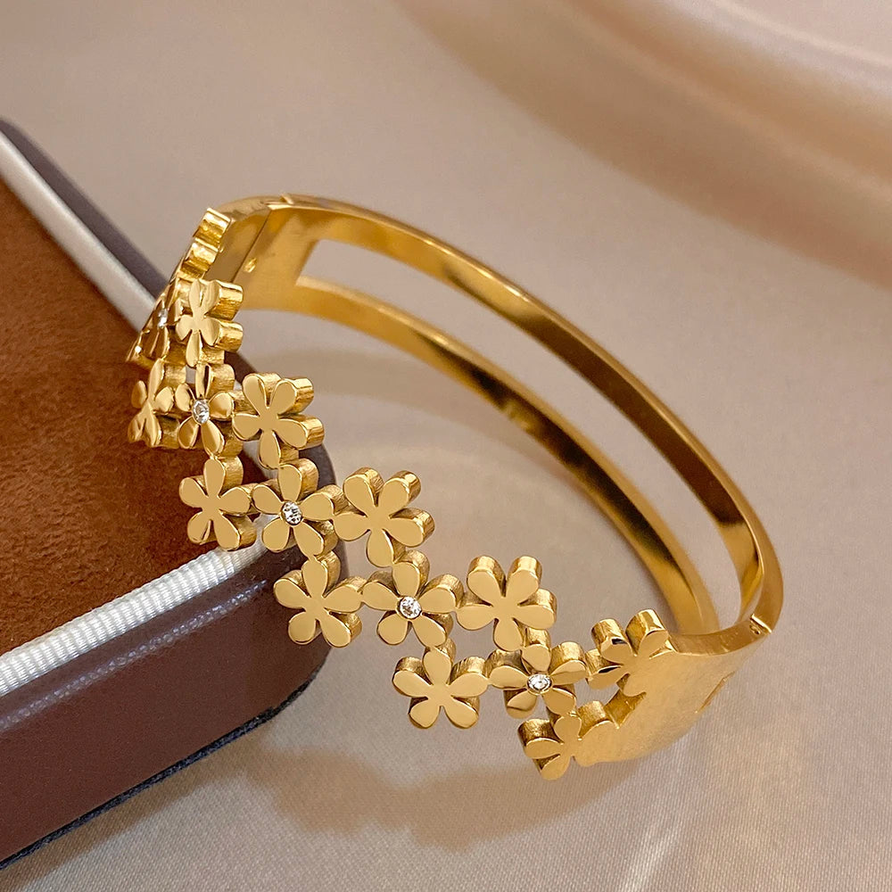 Gold-plated wide cuff bangle with cascading flower charms and small crystal studs