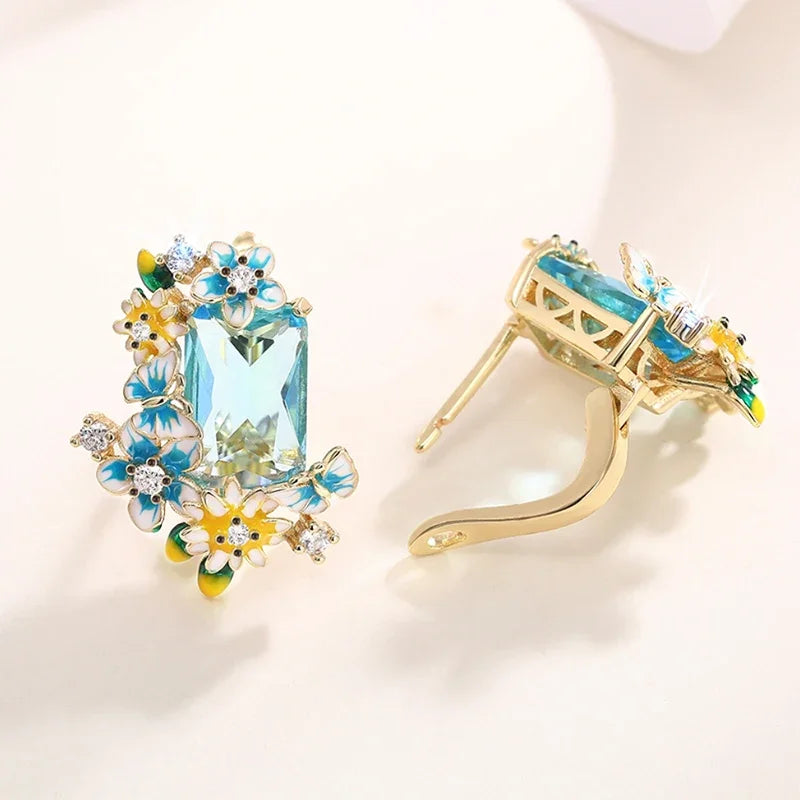Gold-tone floral drop earrings with aqua crystal center and visible hook and back closure